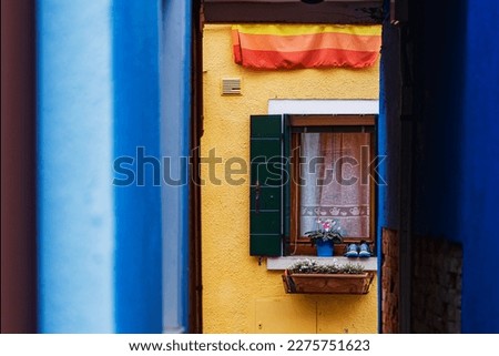 view through a narrow coloured alley to an open window with a yellow wall