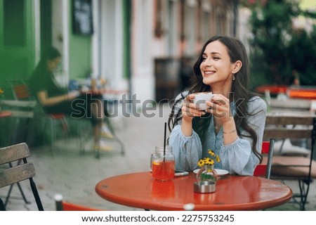 Smiling beautiful young woman sitting in cafe outdoors. Portrait of caucasian female drinking espresso coffee in a romantic garden outside of a cafe. Copy space.