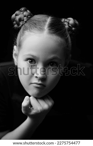 Black and white portrait of a beautiful naughty girl who makes a funny face and looks into the camera. Psychological picture. Children, emotions.