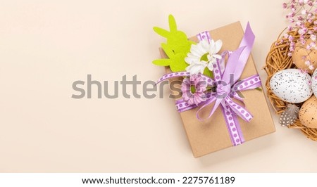 Gift box, Easter eggs and flowers on beige background with space for your greetings. Flat lay