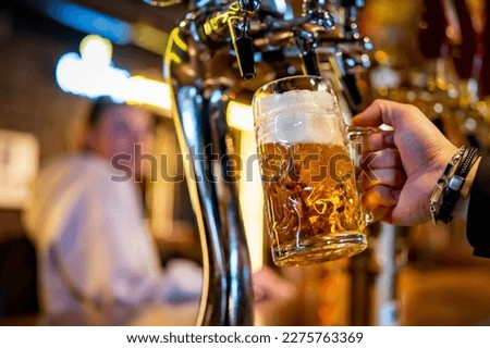 man bartender hand at beer tap pouring a draught beer in glass serving in a restaurant or pub Royalty-Free Stock Photo #2275763369