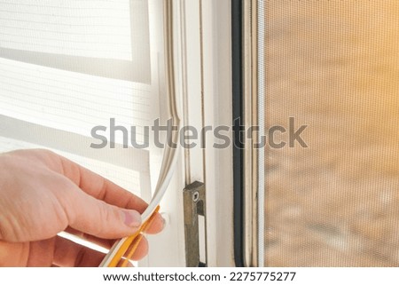 The man wipes the window frame with a degreaser and glues a sealing rubber tape on it for noise insulation, wind protection, weather protection. Royalty-Free Stock Photo #2275775277