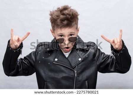 Portrait of a heavy metal boy in sunglasses. Cute teenager in a leather jacket doing a rock and roll sign Royalty-Free Stock Photo #2275780021