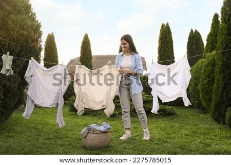 Smiling woman hanging clothes with clothespins on washing line for drying in backyard Royalty-Free Stock Photo #2275785015