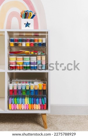 Transparent plastic containers with stationery and supplies for drawing and craft on shelves. White shelving with various material for creativity and art activity. Organizing and storage craft room.  Royalty-Free Stock Photo #2275788929