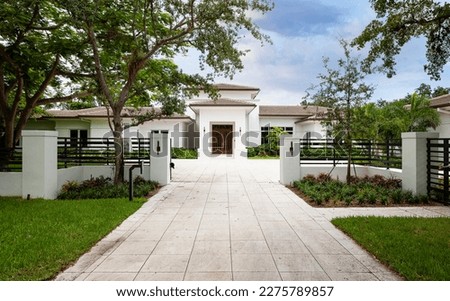 Elegant mansion entrance located in the Pinecrest village, in Miami-Dade, Florida, with large tropical vegetation around it, short grass, driveway, summer weather, trees, palm trees, blue sky Royalty-Free Stock Photo #2275789857