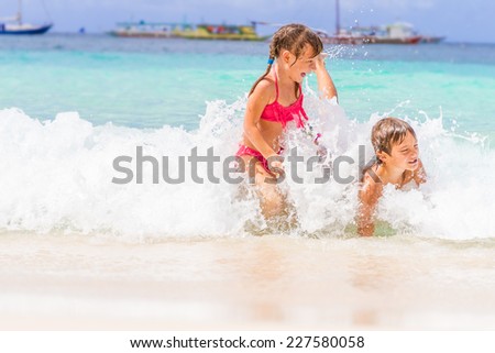 two young happy children - girl and boy - having fun in water, tropical summer vacations, holidays