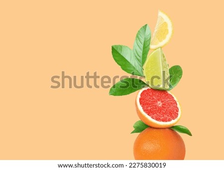 Stack of different fresh citrus fruits with green leaves on pale orange background, space for text