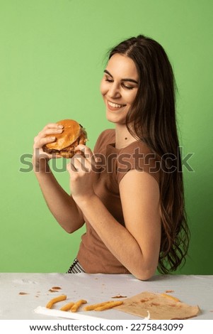 Portrait of a young caucasian woman holding a hamburger and smiling. This is a studio portrait and the background is lime green.