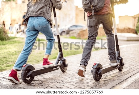 Millenial couple riding electric scooters at urban city park - Genz students using new ecological mean of transportation - Green eco energy concept with zero emission - Warm filter with sunshine halo Royalty-Free Stock Photo #2275857769