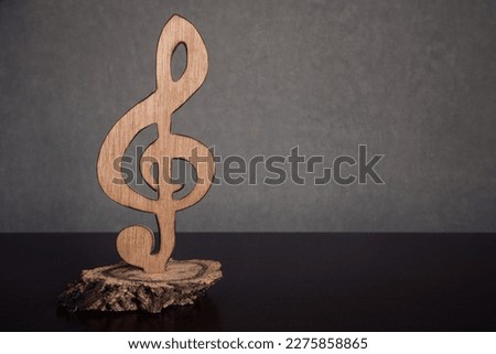 A treble clef statuette carved in wood isolated against a dark background with empty space for text. Symbol of music