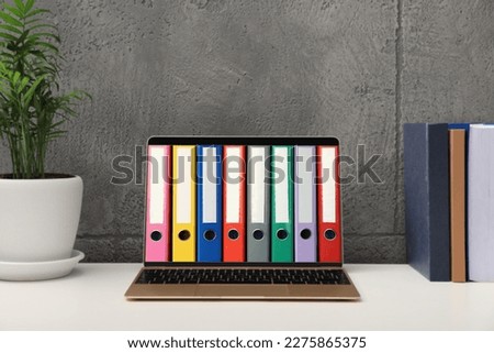 Store and organize information. Modern laptop with hardcover office folders on screen