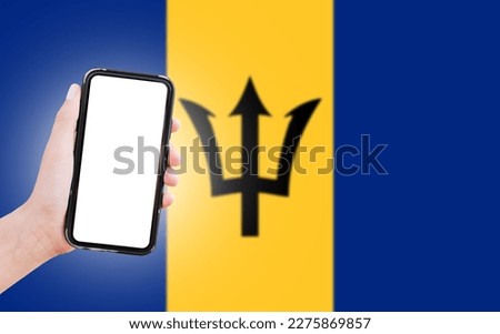 Male hand holding smartphone with blank on screen, on background of blurred flag of Barbados. Close-up view.