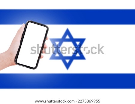 Male hand holding smartphone with blank on screen, on background of blurred flag of Israel. Close-up view.