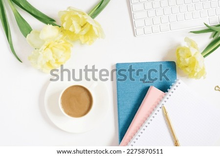 Modern white office desk table with a cup of coffee, computer keyboard, notebooks, pen, flowers and other accessories. Top view with a space to copy on a white background. Top view, flat lay.