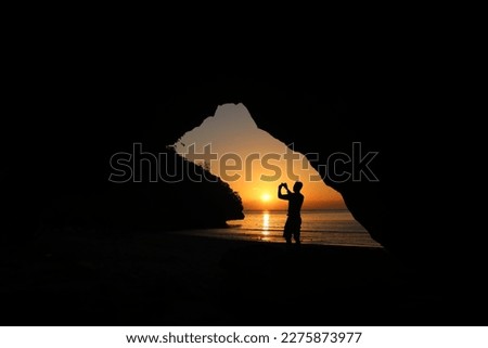 Man taking picture of sunset, beautiful red sky In front of a cave on the beach in Thailand