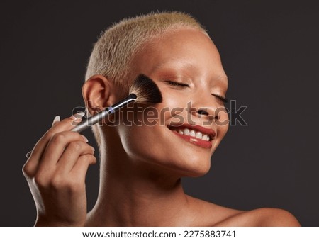 Woman, smile and makeup brush for beauty cosmetics, skincare or facial treatment against a gray studio background. Happy beautiful female model applying cosmetic product on face for self care or love