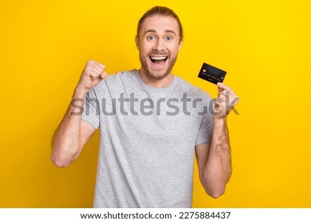 Photo of glad overjoyed man wear trendy grey clothes hold bank card rejoice receive salary isolated on yellow color background