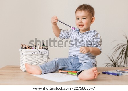 cute baby boy is sitting drawing with pencils on the wooden floor of the house