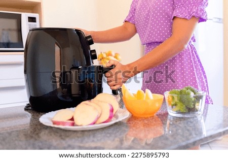 Brazilian woman using air fryer to fry food in home kitchen. Electric fryer without oil Royalty-Free Stock Photo #2275895793