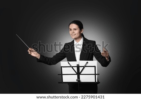 Happy professional conductor with baton and note stand on black background