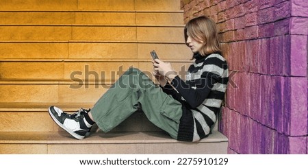 Young pretty woman in a striped black and white sweater, social media influencer, sitting on stairs of the building city using smartphone.