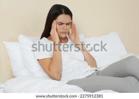 Young woman suffering from headache on bed indoors. Hormonal disorders Royalty-Free Stock Photo #2275912381