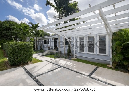 Facade of an elegant and modern wooden house in the West Flagler neighborhood, in Little Havana, driveway, short grass, privet walls, path to the front door, trees and palm trees, streets, light blue 