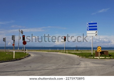 A crossroads with traffic lamps and direction signboard. Traffic lamps are red and siignboard is blanked. Road at coastline in a beautiful day with blue sky. Blue and white traffic signboard.
