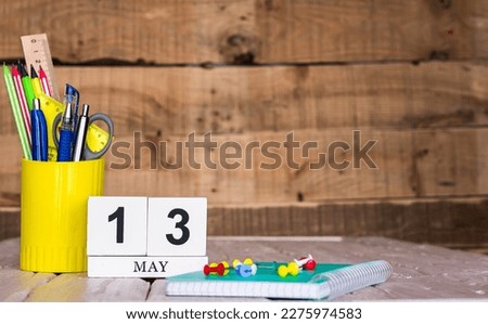 May calendar background with number  13. Stationery pens and pencils in a case on a wooden vintage background. Copy space notepad with pencils and calendar. Planner place for text.
