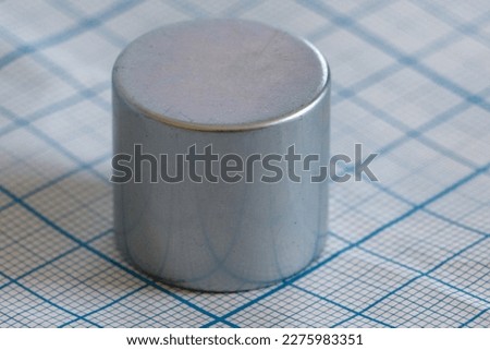 Neodymium cylindrical magnet clous up. It is located on graph paper with blue stripes. Selective focus. Copy space Royalty-Free Stock Photo #2275983351