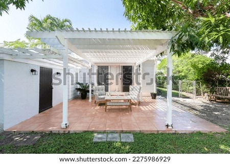 Beautiful patio with a wooden shed, with armchairs and an outdoor table in the West Flagler neighborhood, in Little Havana, short grass, privet walls, trees and palm trees, light blue walls and blue s