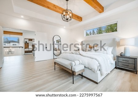 Primary master bedroom with wood beam ceiling hardwood floors white walls sitting area with comfortable chair and books on shelves near staircase with glass walls and wrought iron rails upstairs rooms
