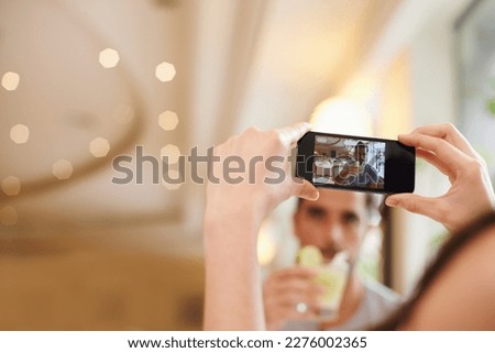 Taking a pic of her special man having a cocktail. A woman taking a picture of her partner while dining out at a fancy restaurant.