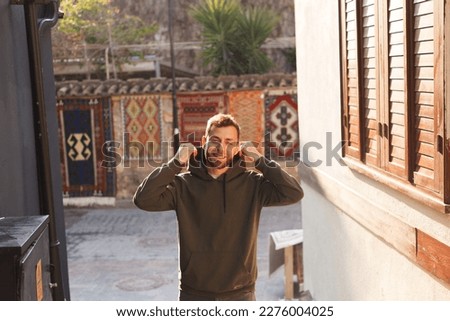 young man with a beard in a hoodie on a narrow street in the city, sunlight