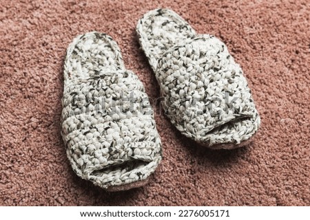 White knitted handmade slippers stand on a red carpet, close-up photo