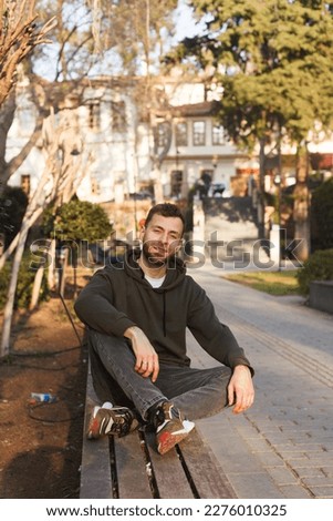 young man with a beard in a hoodie in the city, sunlight