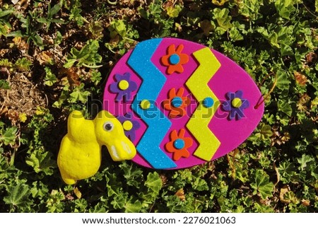 Easter yellow bunny, wood flower and an Easter card on the green grass. Beautiful picture with a handmade rabbit for Easter and an Easter gift bag