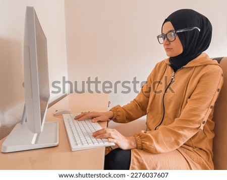 A young woman in hijab wearing a glasses working on a computer laptop at home office. High quality photo