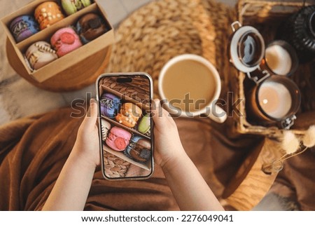 Girl taking a top-down photo of macaron box with various assortment using her phone.