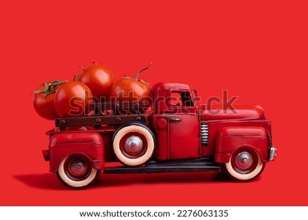 The red truck delivers fresh tomatoes. Vintage red toy truck on a red background.