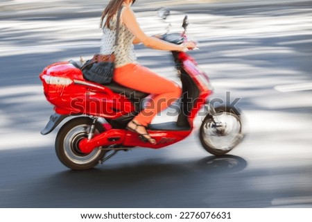 picture with camera made motion blur effect of a young woman riding a red scooter on a street