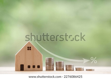 Model wooden house in front of a natural green backdrop and an arrow showing a falling rate of interest. Strategic ideas to get lower interest rates when buying and mortgage a home. Royalty-Free Stock Photo #2276086425