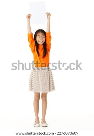 Portrait full body cutout isolated studio shot of Asian young happy primary schoolgirl model in casual outfit standing holding advertising placard paper board for text copy space on white background.