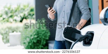 Focus electric car charging at home charging station with blurred progressive man walking in the background. Electric car using renewable clean for eco-friendly concept. Royalty-Free Stock Photo #2276106137