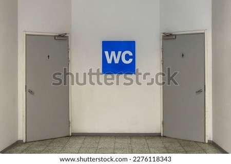 Blue WC sign on the white wall with two toilet doors on each side Royalty-Free Stock Photo #2276118343