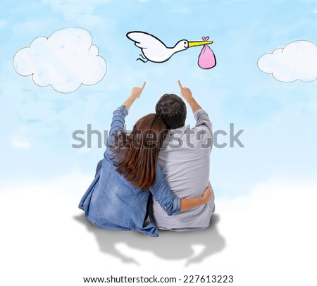 young attractive Hispanic couple on floor, pregnant woman sitting together handsome husband and flying stork bringing baby in pregnancy and family growth concept Royalty-Free Stock Photo #227613223