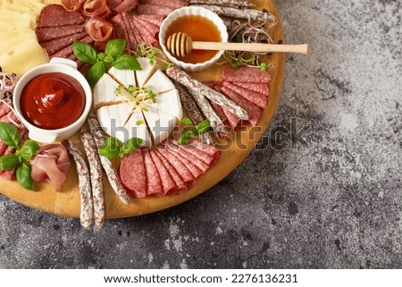 Wooden plate with delicacies. Brie cheese, blue cheese, salami, prosciutto on a wooden board. sausage, cheese, honey. plate of delicacies Royalty-Free Stock Photo #2276136231
