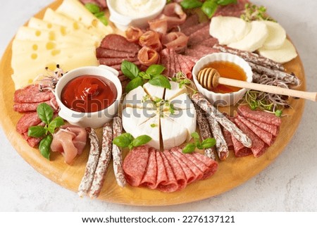 Wooden plate with delicacies. Brie cheese, blue cheese, salami, prosciutto on a wooden board. sausage, cheese, honey. plate of delicacies Royalty-Free Stock Photo #2276137121