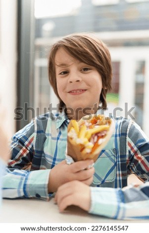 Cute white boys stock photos. Happy little boy holding gyros wrap in hands. Portrait of cheerful white kid eating Greek fast food in a cafe